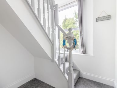 A staircase with white wooden banisters and grey carpet and a window with curtains in Barwood View Torquay
