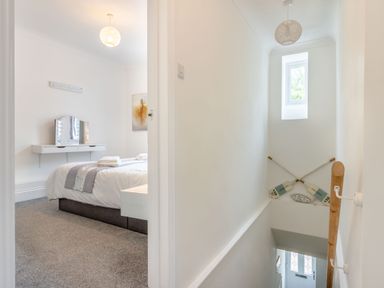 A hallway with a small window above crossed oars and a bedroom with a bed mirror and painting at Barwood View in Torquay