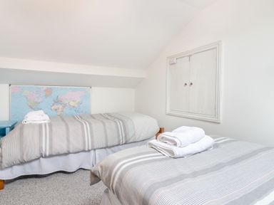 A bedroom with two single beds striped bedding a world map on the wall and folded towels on the beds at Barwood View in Torquay