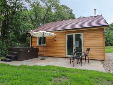 Wooden cabin with a hot tub umbrella and outdoor chairs on a patio at Park Brook Dell in Scorton