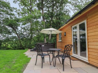 A patio with two black metal chairs a round table and an umbrella next to a wooden house at Park Brook Dell in Scorton