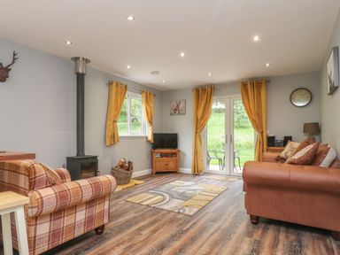A living room with a wood stove armchairs a TV on a wooden stand and yellow curtains at Park Brook Dell in Scorton
