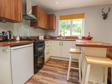 A kitchen with wooden countertops white cabinets two stools and a window at Park Brook Dell in Scorton