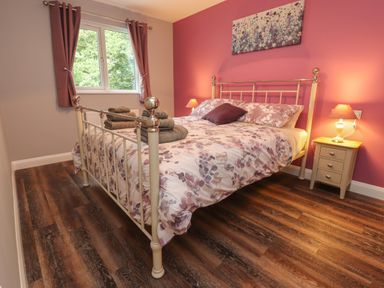 A bedroom with a bed with floral bedding bedside tables lamps curtains on window and a painting on wall at Park Brook Dell in Scorton