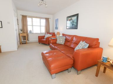 A living room with orange leather sofa and chair beige carpet and wooden side tables at Fairways in Wyke Regis