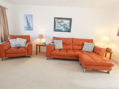 A living room with orange leather sofas side tables with lamps and framed pictures on the walls at Fairways in Wyke Regis