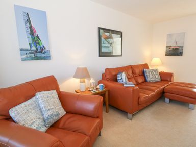 A living room with two leather sofas a wooden side table with a lamp mugs and pictures of sailboats on the wall at Fairways in Wyke Regis