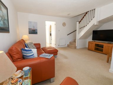 A living room with a brown leather sofa a television on a wooden stand and carpeted stairs at Fairways in Wyke Regis