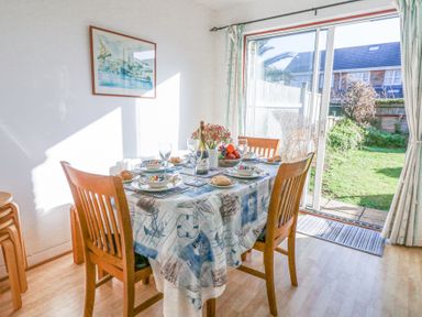 A dining area with a set table and wooden chairs next to sliding glass doors opening to a garden at Fairways in Wyke Regis