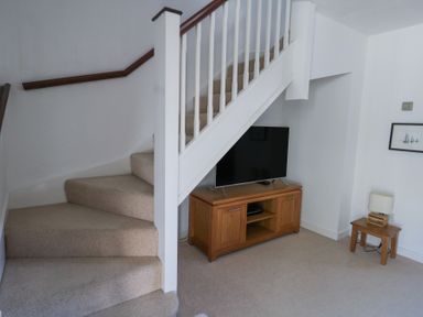 A carpeted staircase next to a wooden TV stand with a television on it and a wooden side table with a lamp at Fairways in Wyke Regis