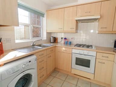 A kitchen with wooden cabinets a washing machine a sink a gas stove an oven and kitchen utensils on the counter at Fairways Wyke Regis