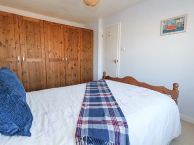 A bedroom with a wooden wardrobe a bed with white bedding blue pillows and a plaid blanket on the bed at Fairways Wyke Regis