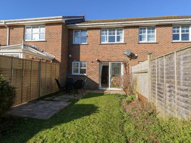 A backyard with a lawn and patio furniture beside a brick house with sliding glass doors and windows at Fairways in Wyke Regis