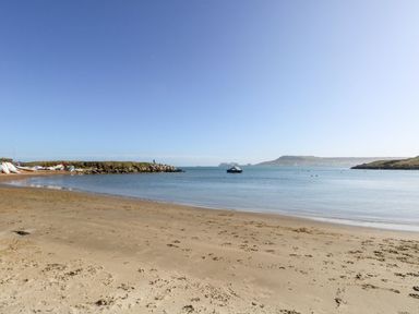 A sandy beach with footprints a calm sea a boat and people standing on a rocky outcrop at Fairways in Wyke Regis