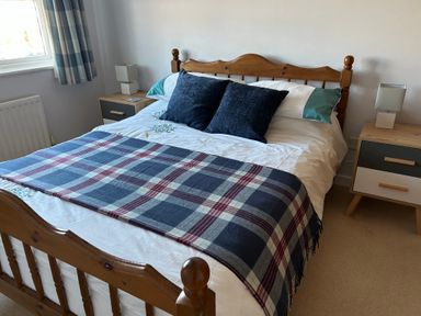 A bedroom with a wooden bed frame blue plaid blanket and two bedside tables with lamps at Fairways in Wyke Regis