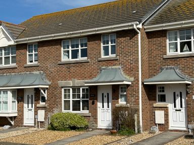 A row of brick townhouses with white doors and windows under a blue sky at Fairways in Wyke Regis