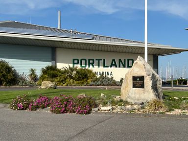 Exterior of Portland Marina building with large rock and plaque in front and boats in background at Fairways in Wyke Regis
