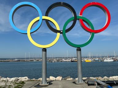 A waterfront view with large Olympic rings sculpture and boats docked at a marina in the background