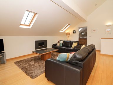A living room with two black leather sofas a coffee table a rug a fireplace and skylights at Cholwell Barn Apartment Mary Tavy