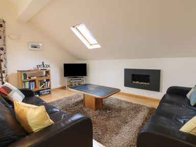 A living room with two black sofas a wooden coffee table a rug and a TV at Cholwell Barn Apartment in Mary Tavy