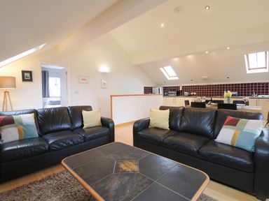 A living room with two black leather sofas and a coffee table next to a kitchen with dining table at Cholwell Barn Apartment Mary Tavy
