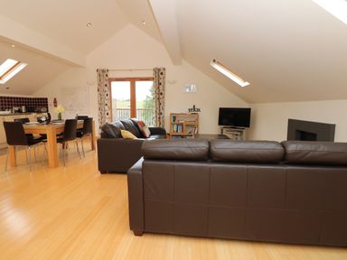 A living room with brown leather sofas a dining table with chairs and a TV at Cholwell Barn Apartment in Mary Tavy