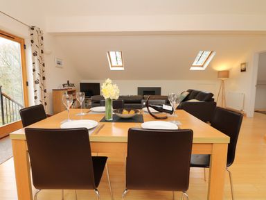 A dining table set with plates glasses and a flower vase in a living room with sofas and skylights at Cholwell Barn Apartment Mary Tavy