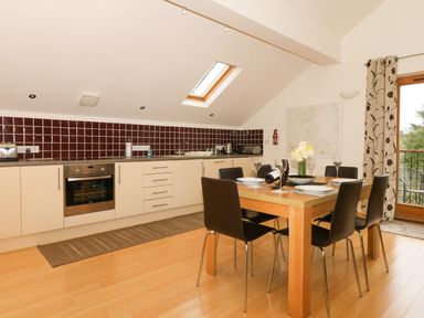 A kitchen with a dining table and six chairs with dinnerware and flowers at Cholwell Barn Apartment in Mary Tavy