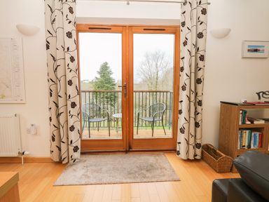 A living room with glass doors leading to a balcony with two chairs and a table at Cholwell Barn Apartment in Mary Tavy