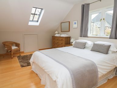 A bedroom with a double bed a wooden dresser a wicker chair a skylight window and a window with curtains at Cholwell Barn Apartment Mary Tavy