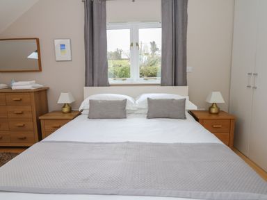 A bedroom with a double bed with white and gray bedding between wooden bedside tables with lamps at Cholwell Barn Apartment in Mary Tavy