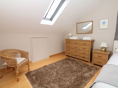 A bedroom with a wicker chair a dresser with a mirror and a bedside table with lamps at Cholwell Barn Apartment in Mary Tavy