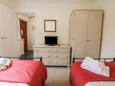 A bedroom with two single beds covered in red blankets and white towels on top a dresser with a small tv and a mirror above it and a wardrobe at Cholwell Barn Apartment Mary Tavy