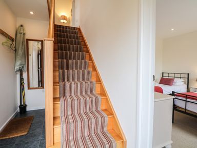 A stairway with striped carpet leading upstairs and a bedroom with beds visible through an open door at Cholwell Barn Apartment in Mary Tavy