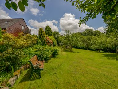 A garden with a wooden bench and various trees near a house at Cholwell Barn Apartment in Mary Tavy