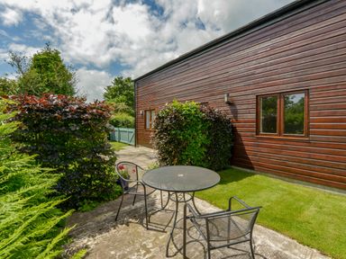 An outdoor patio with metal table and chairs next to a wooden building and garden at Cholwell Barn Apartment in Mary Tavy