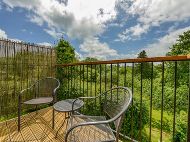 A balcony with two metal chairs and a small round table overlooking trees and greenery at Cholwell Barn Apartment in Mary Tavy
