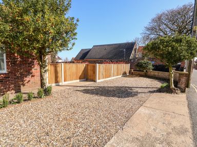 A gravel driveway with two trees near a brick wall and wooden fencing at Sunnyside in Wells-Next-The-Sea