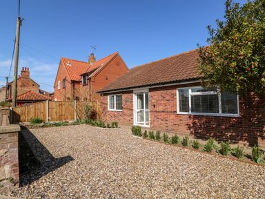 A single-story brick house with a gravel driveway and small plants along the edge at Sunnyside in Wells-Next-The-Sea