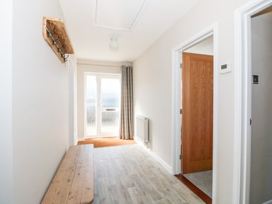 A hallway with a wooden bench and hooks on the wall near a glass door at Sunnyside in Wells-Next-The-Sea