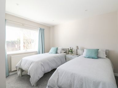 A bedroom with two single beds a nightstand with a lamp and flowers and a window with curtains at Sunnyside in Wells-Next-The-Sea