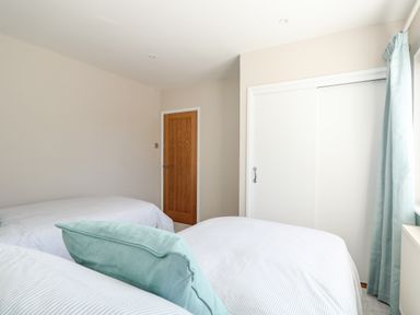 A bedroom with two beds a wooden door a white closet and a window with curtains at Sunnyside in Wells-Next-The-Sea