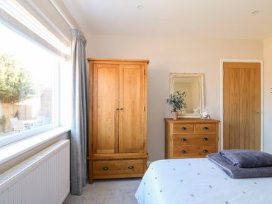 A bedroom with a wooden wardrobe wooden chest of drawers a mirror a bed with folded towels by the window at Sunnyside in Wells-Next-The-Sea
