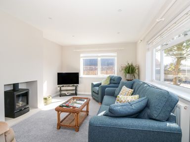 A living room with blue sofa and armchair a television and a wicker coffee table at Sunnyside in Wells-Next-The-Sea