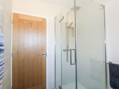 A bathroom with a wooden door a glass shower enclosure and towels at Sunnyside in Wells-Next-The-Sea