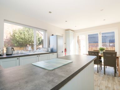 A kitchen with a countertop island a dining table with chairs and large windows at Sunnyside in Wells-Next-The-Sea