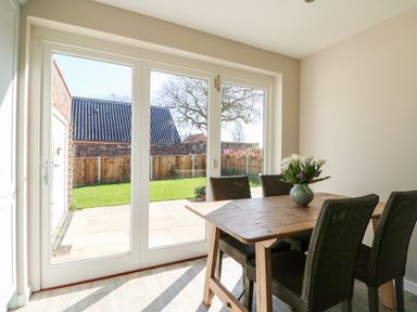 A dining area with a wooden table and four chairs next to glass doors opening to a garden at Sunnyside in Wells-Next-The-Sea