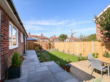 A backyard with a paved patio, lawn, wooden fence, garden plants, and an outdoor table with chairs at Sunnyside in Wells-Next-The-Sea