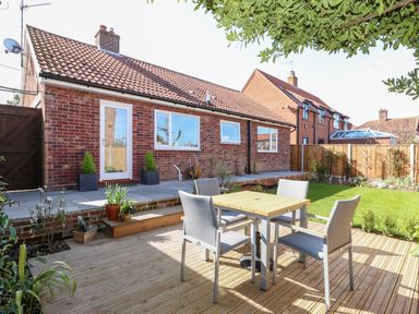 A backyard with a wooden table and four chairs on a deck next to a brick house with tiled roof at Sunnyside in Wells-Next-The-Sea