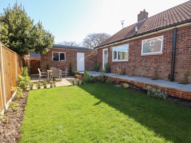 A backyard with a lawn table and chairs along a wooden fence and a brick house at Sunnyside in Wells-Next-The-Sea